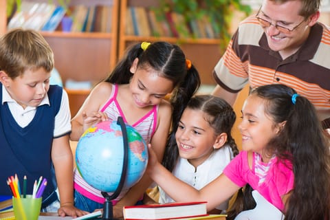 Young students looking at globe with their teacher