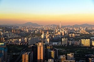 The skyline in Shenzhen, a megacity in China. There are skyscrapers in the foreground with mountains and a sunset in the far background.