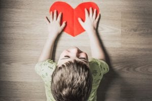 Young smiling child with hands on a paper heart