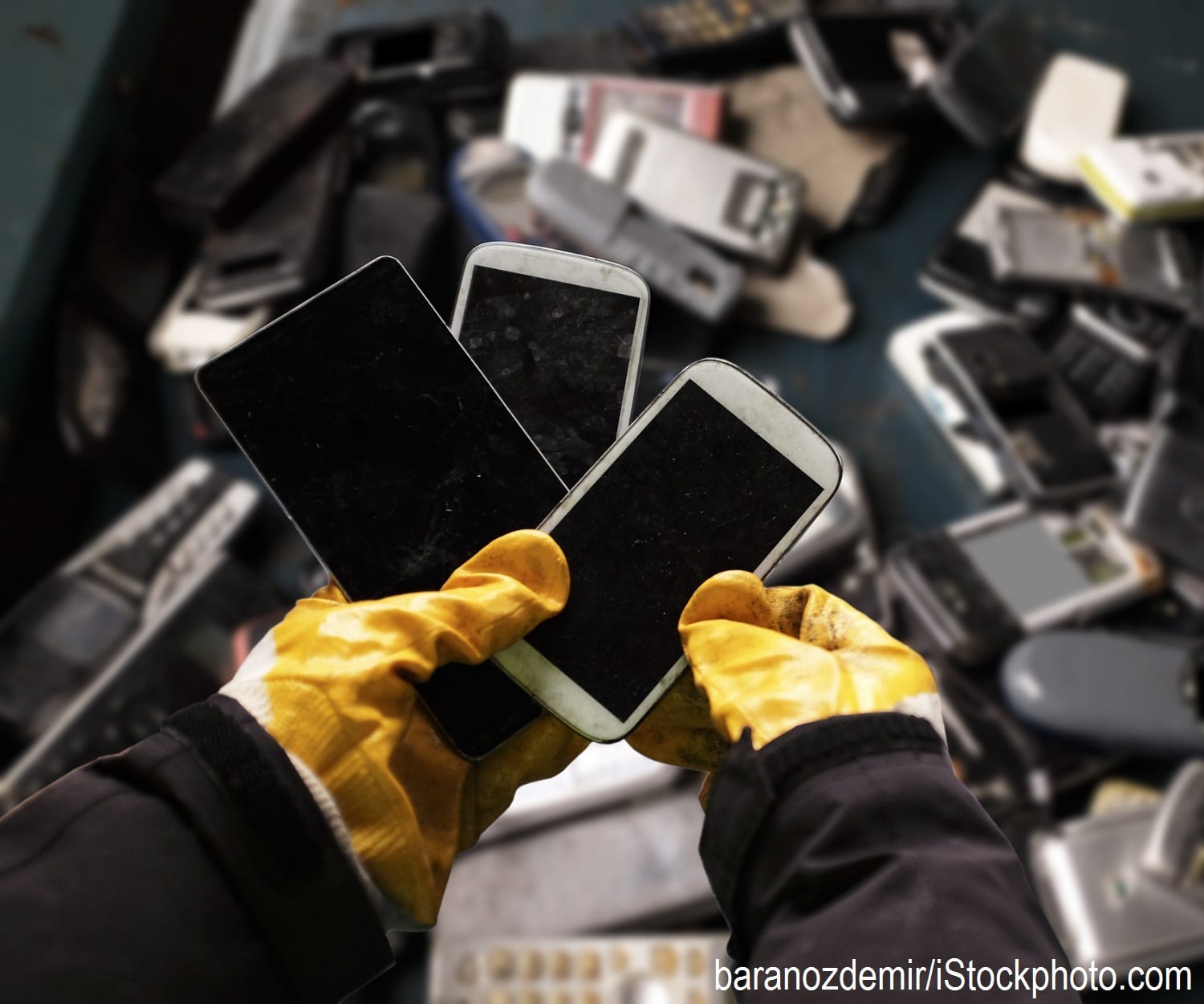 A worker holding cell phones and other electronics, e-waste ready to be recycled.