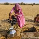 An Indian woman drawing water from a well while her children wait beside her.