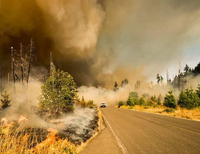 Car drives away from climate-fueled wildfire in Lowell, California, US