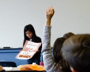 Girl presents poster to class while student raises hand
