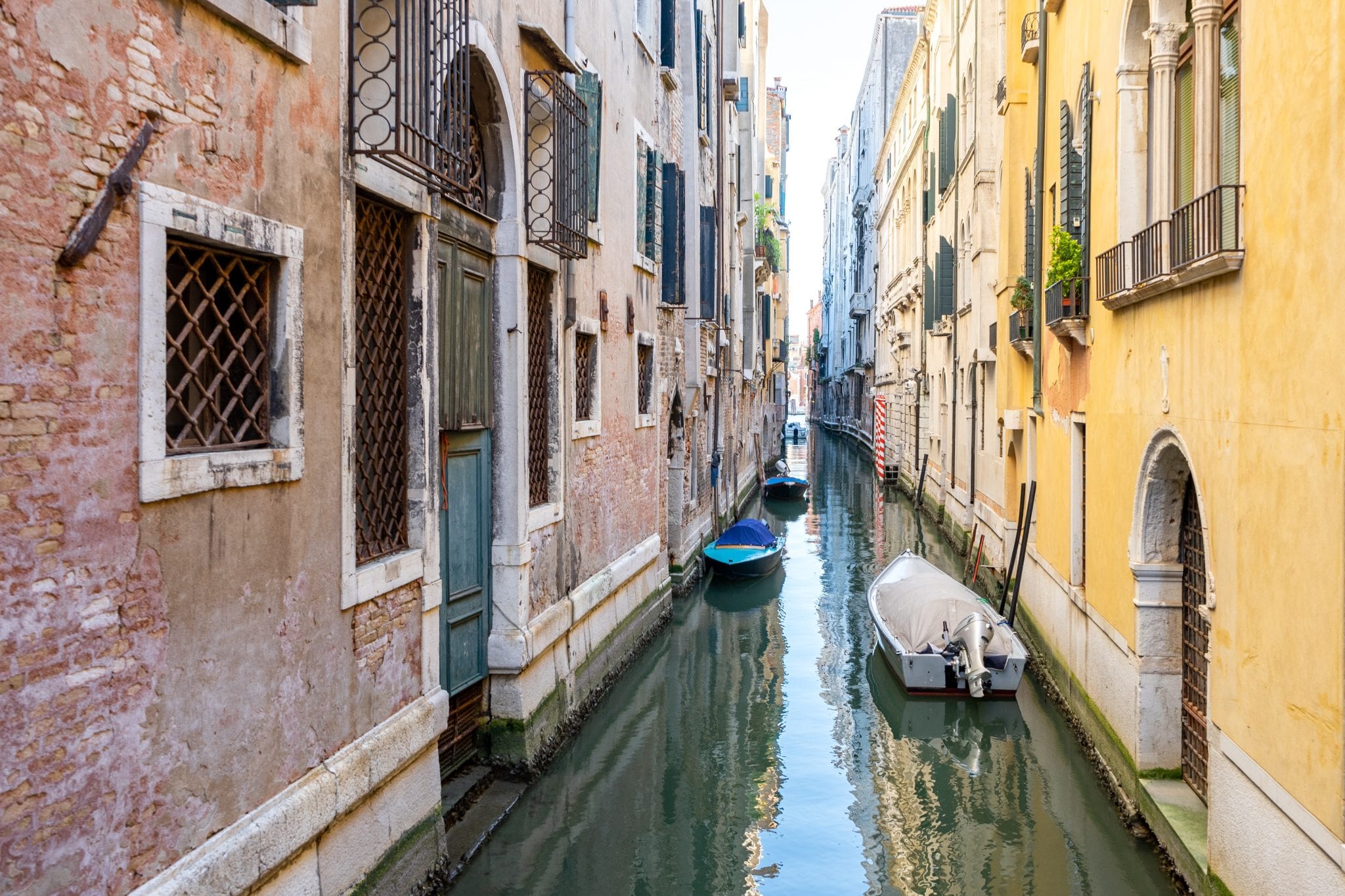 White and blue boats on canal between concrete buildings in Venice, Italy