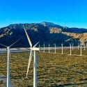 White wind turbines on brown sand with mountains in background