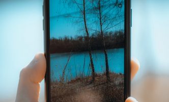 Hand holding smartphone taking photo of lake