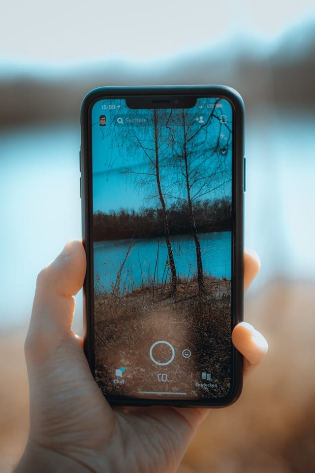 Hand holding smartphone taking photo of lake