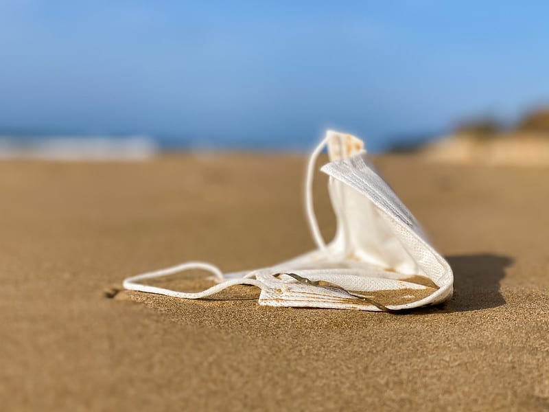 Close up view of a white, single use face mask discarded on the beach