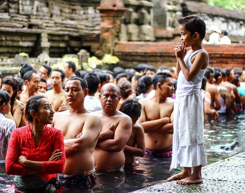 A crowd of people wait in line in the water at Tirta Empul temple in Bali, Indonesia