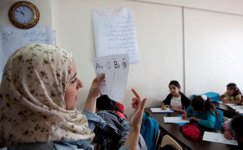 Syrian children sit at desks while teacher presents a worksheet as part of informal education and integration courses