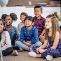 Young, smiling children sit cross-legged on a classroom carpet