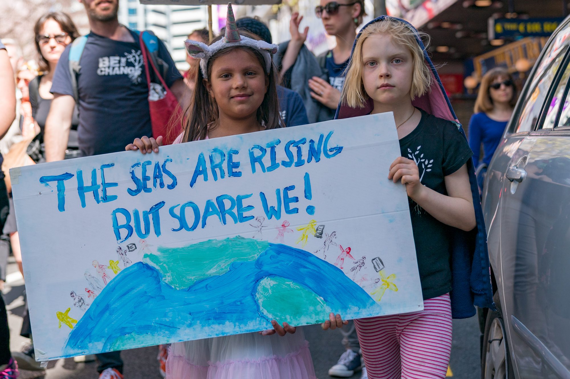 Young girls hold colorful protest sign that reads: The seas are rising but so are we!