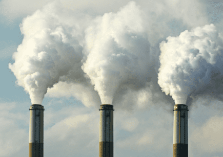 Three smokestacks emit fumes up into a cloudy blue sky