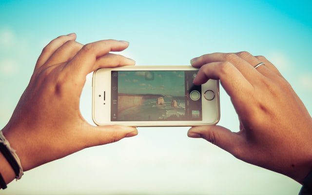 Hands hold an iPhone in landscape mode, photographing a beach scene