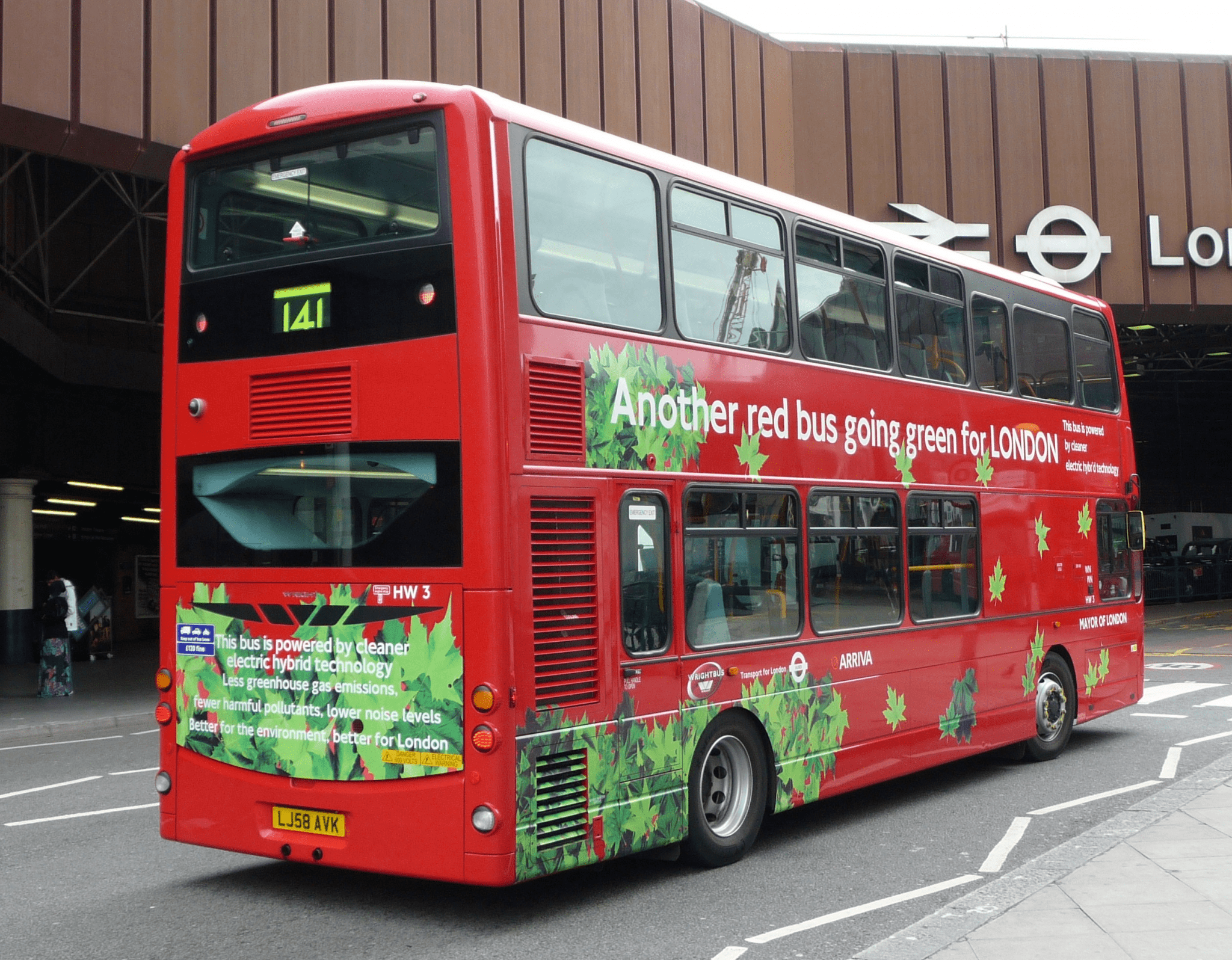 A bright red, hybrid double decker moves down a London street