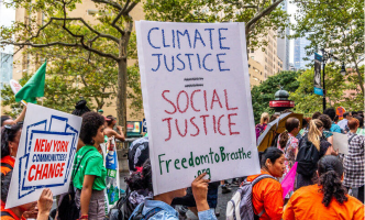 People march along a city street holding signs for climate justice, social justice, and change in New York communities