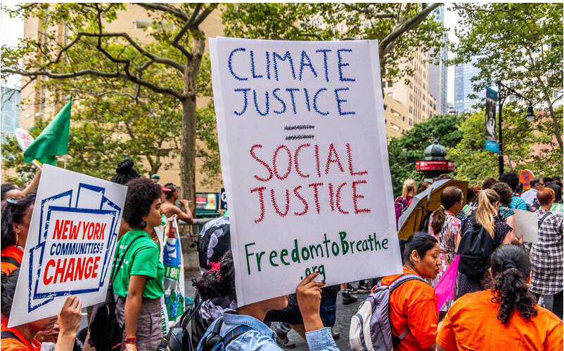 People march along a city street holding signs for climate justice, social justice, and change in New York communities