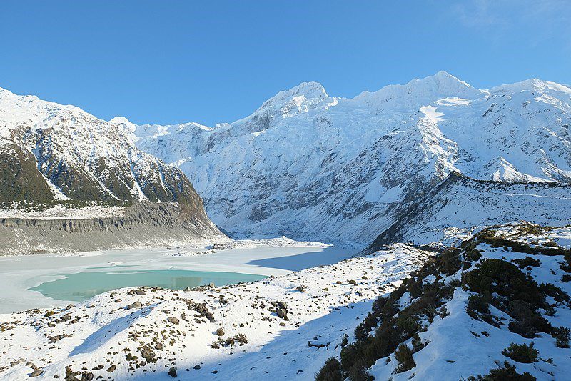 Snow capped mountains surround a partially frozen and snow-covered lake