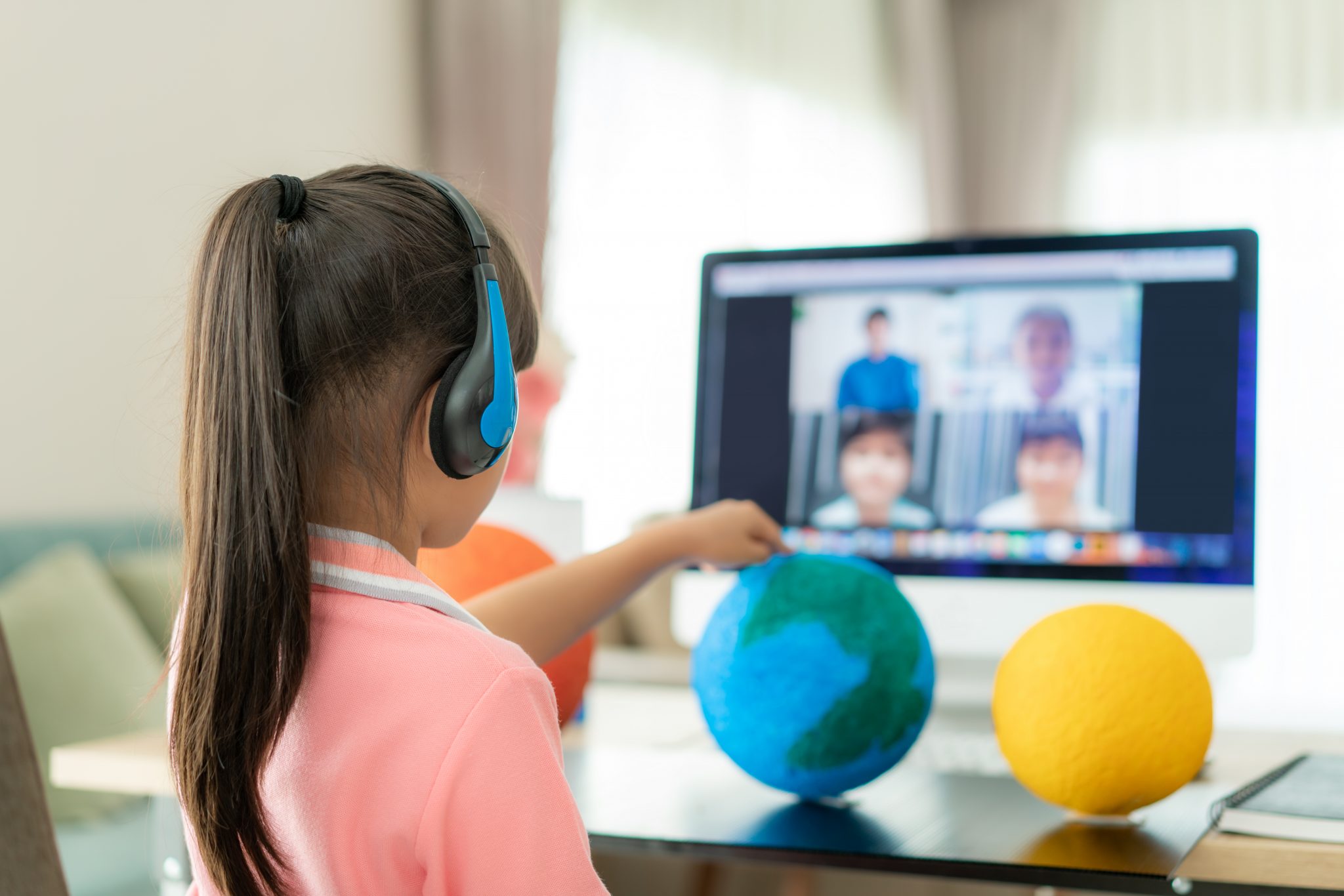 A young girl presents a solar model project to her teacher and other classmates via a virtual learning video conference