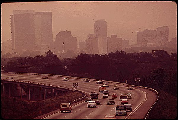 A sepia toned photo shows a highway stretching in front of Birmingham, Alabama's skyline, which is obscured by smog