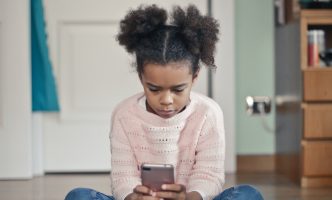 Young girl sits in her house and plays on a smartphone.