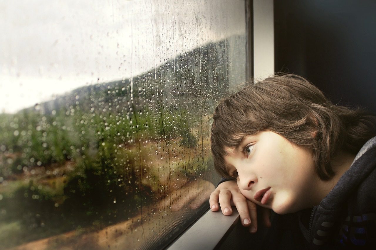 Young boy looking out window to a rainy day