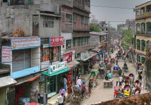 A street view in Lalbagh, Dhaka shows a busy street with lots of foot traffic. Lalbagh is one of the densest neighborhoods in the world and is known for its Chawk Bazaar.