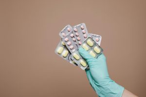  A hand in a latex glove holds blister packs of different medicines.