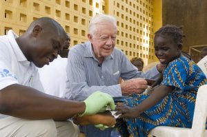 President Carter tries to comfort a young girl as a Carter Center volunteer dresses her painful guinea worm wound. 