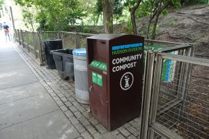 A community composting bin next to recycling and trash cans in New York.