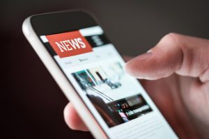 A close-up of a hand holding a phone and scrolling through a news site.