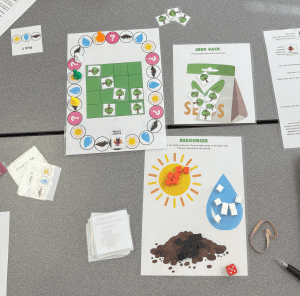 An overhead shot of students playing Lessons from the Lorax, with the gameboard, playing cards, and resource banks visible.