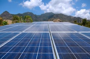 Solar panels in Indonesia, with a lush mountain range in the background.