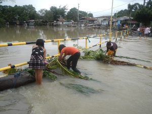 Three Filipino children remove debris from the road after Typhoon Vamco, a natural disaster that exacerbated food insecurity in the country.