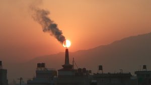  A factory smokestack is silhouetted in front of a setting sun. 