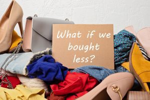 A sign on a pile of fast fashion clothing says, "What if we bought less?"