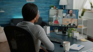 A woman in a home office attends a virtual meeting with colleagues. 